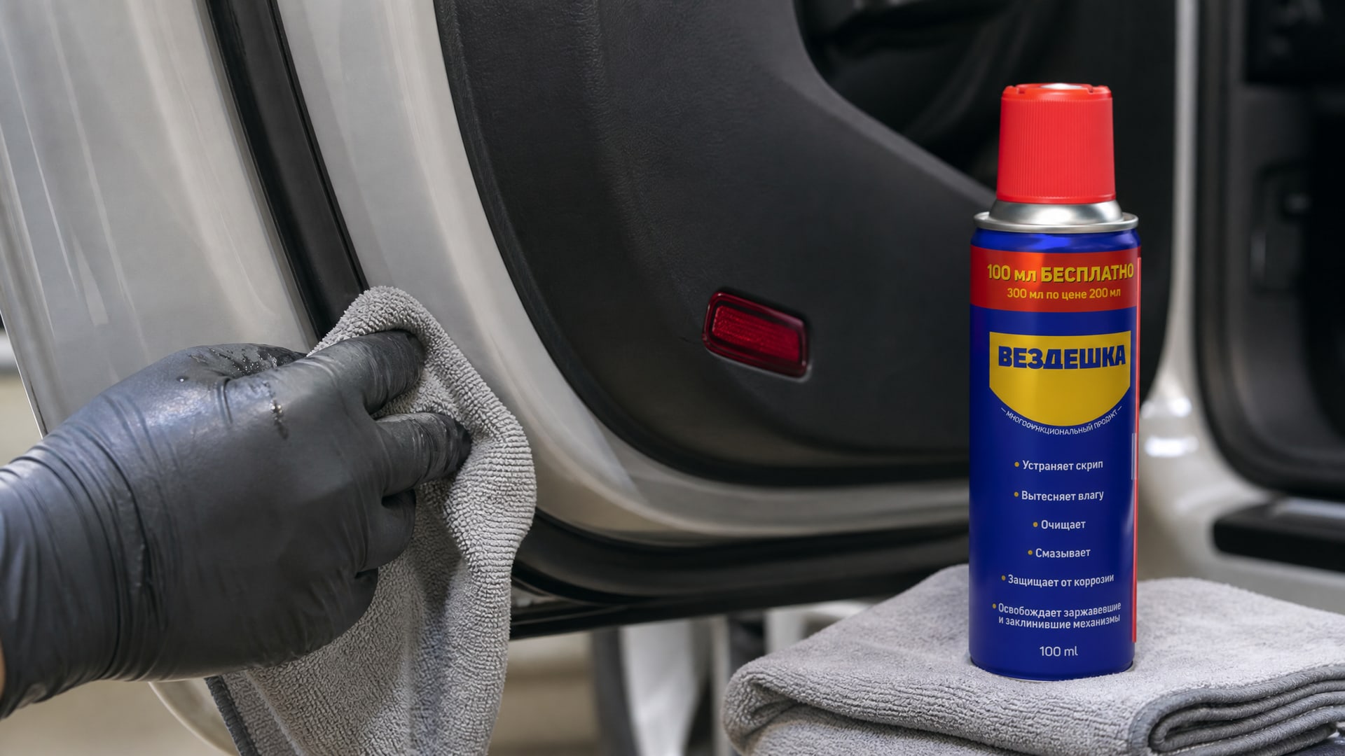 Человек в перчатке наносит универсальную смазку WD-40 на уплотнитель двери.