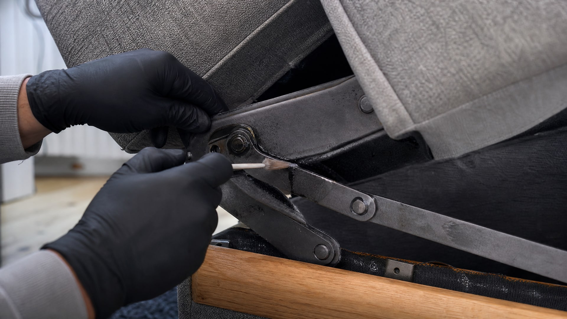 Руки наносят WD40 на петлю складного механизма дивана в домашней обстановке.