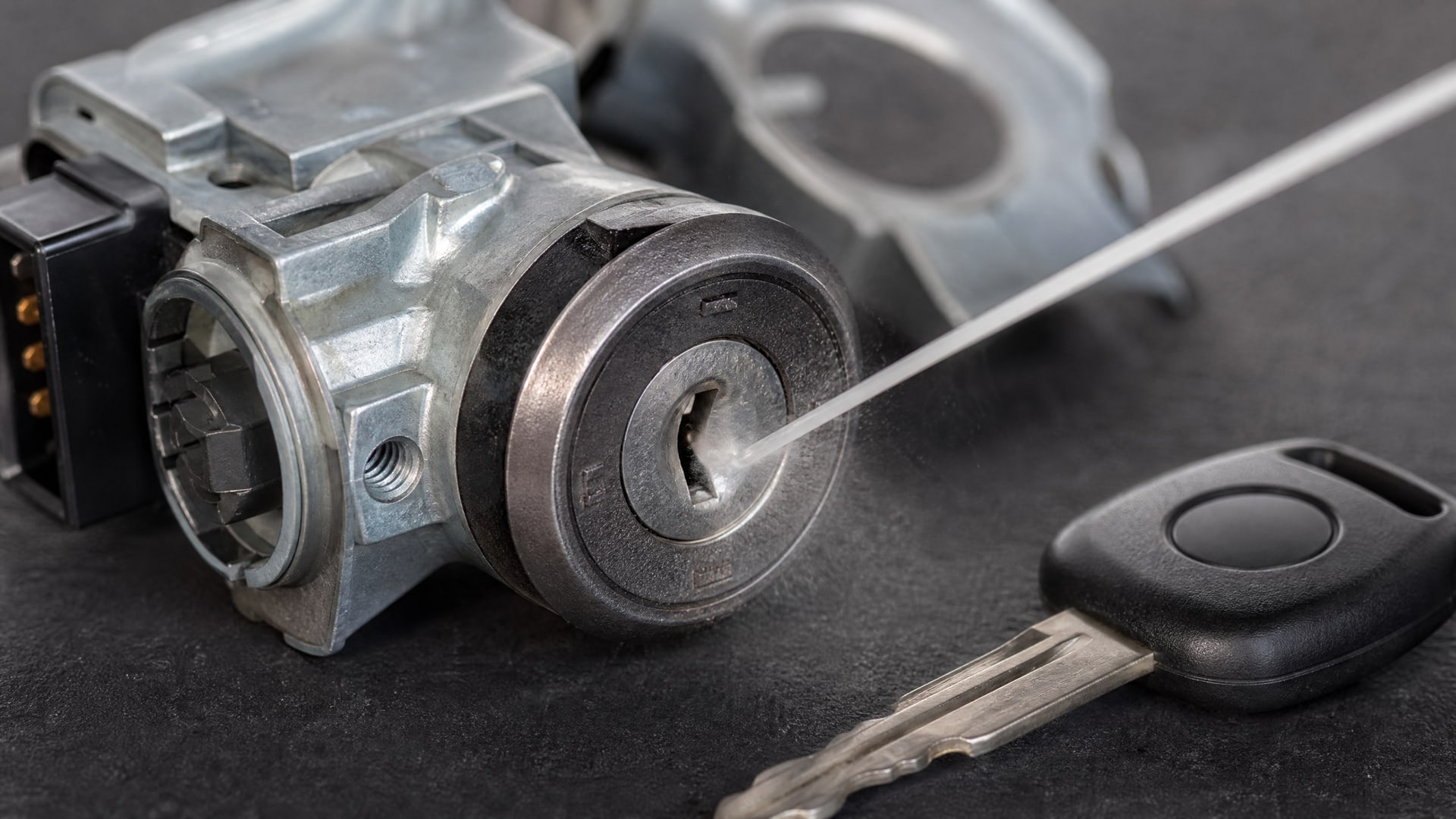 В замок зажигания автомобиля тонкой трубочкой распыляется WD40, рядом лежит ключ.