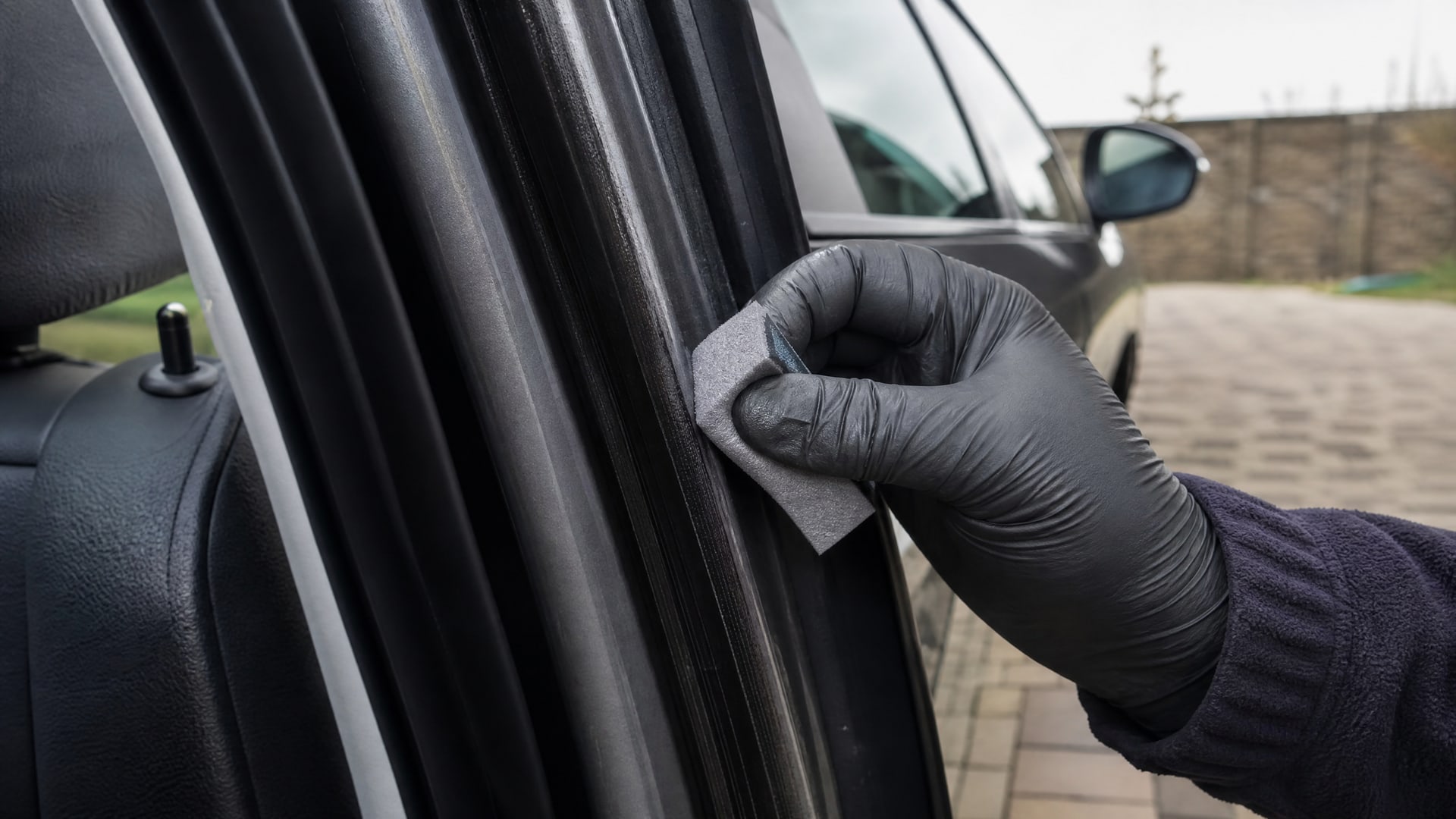 Нанесение прозрачной смазки на черный уплотнитель автомобильной двери рукой в перчатке.