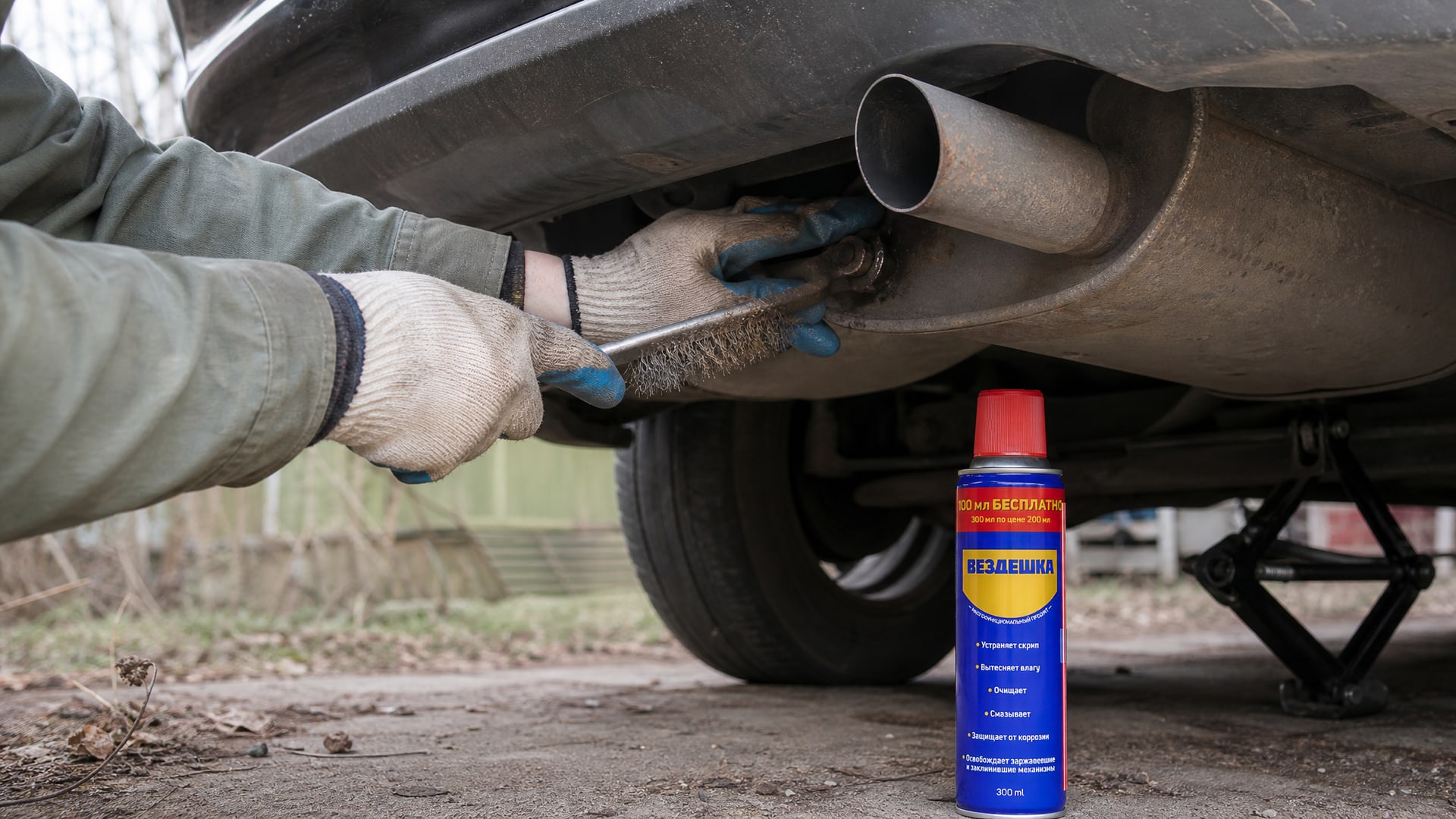 Рука наносит смазку WD40 на закисшие болты глушителя.