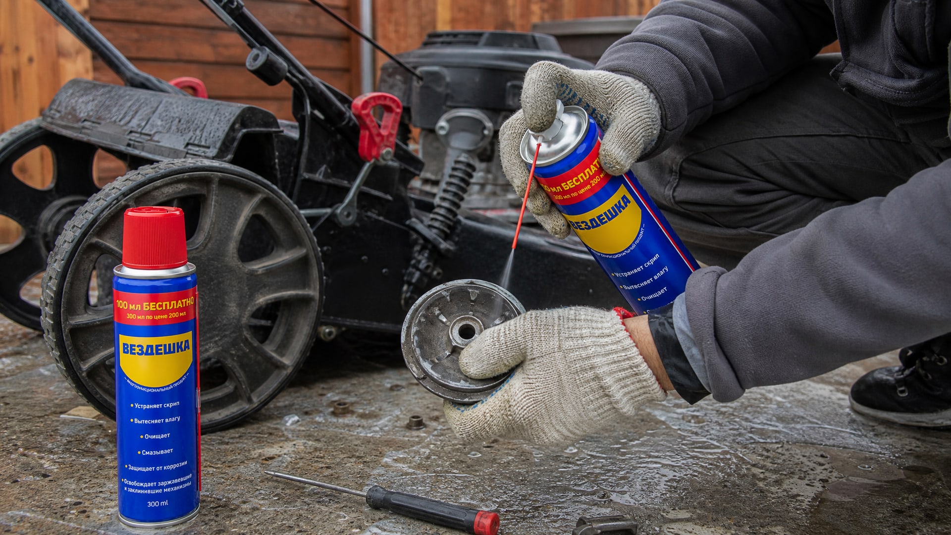 Рука в перчатке наносит универсальную смазку WD-40 на газонокосилку.