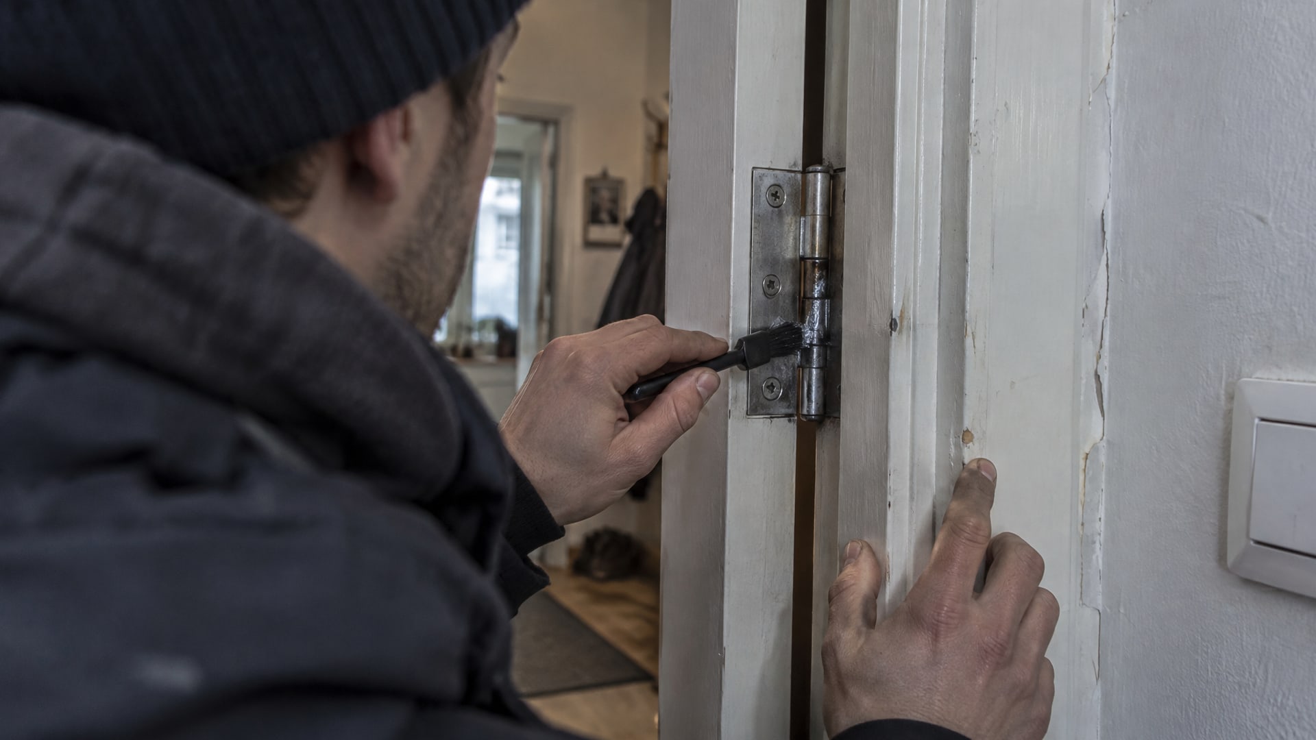 Человек смазывает петлю межкомнатной двери силиконовой смазкой, видны только руки.