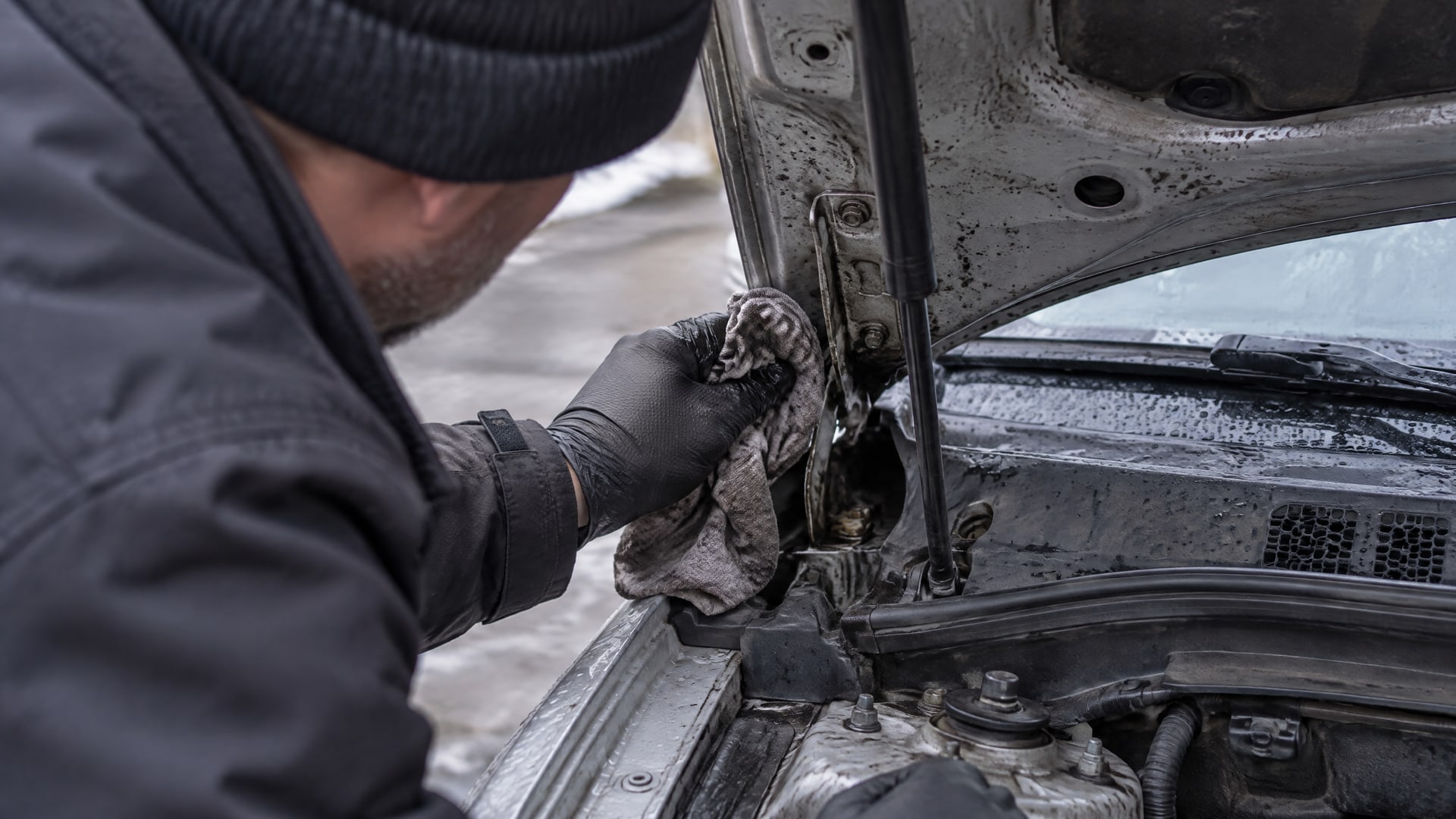 Перчатка удаляет старую грязную смазку с петли капота автомобиля.