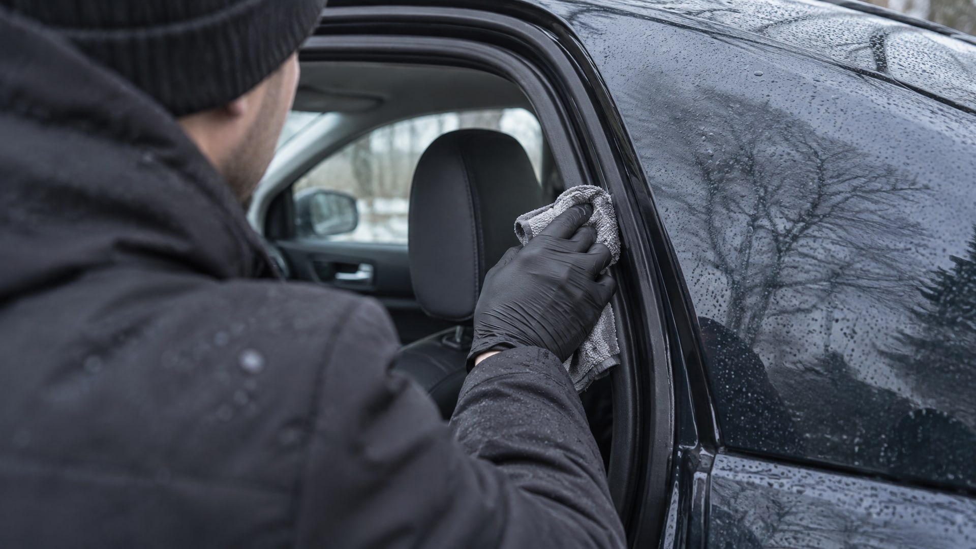 Рука в перчатке тщательно протирает влажной тряпкой резиновый уплотнитель автомобильной двери.